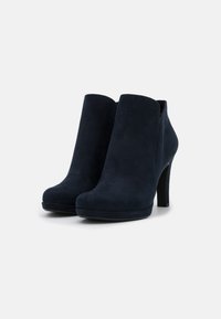 Botas de tobillo de ante azul marino con una textura suave, punta redonda y tacón alto. El diseño presenta una silueta elegante y acentos minimalistas.