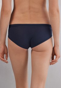 Navyblauwe bikini onderkant gemaakt van een gladde stof, met een lage snit en naadloze randen voor een strakke uitstraling. Achteraan is een snug fit zichtbaar.