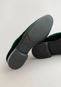 Green velvet shoes with a rubber sole, featuring a textured black base and square-shaped accents on the sole.