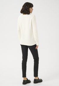 Maglione bianco a coste con maniche lunghe, vista posteriore. Abbinato a pantaloni neri slim-fit e scarpe chunky nere. Design semplice e minimalista.