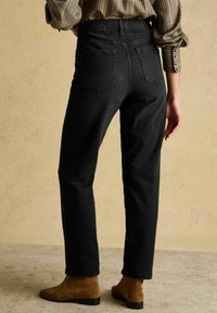 Čierne džínsy z denimu s vysokým pásom a rovnými nohavicami, s dvoma zadnými vreckami, nosené so šekom košeľou a hnedými členkovými topánkami.