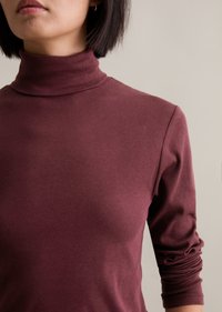 Burgundy turtleneck top with ribbed texture; fitted design with long sleeves and gathered detailing at the cuffs.