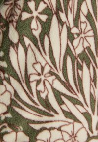 Květnatý vzor látky s krémovými květinami a listy obrysem v hnědé barvě na olivově zeleném pozadí.