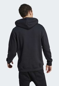 Crna dukserica s teksturiranim materijalom, velikom kapuljačom i rebrastim manžetama i donjim rubom. Jednostavan dizajn bez vidljivih logotipa ili uzoraka.