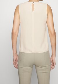 Beige ärmelloses Top mit einem Ausschnitt im Rückenteil, aus einem glatten Stoff, der einen subtilen Glanz aufweist und eine lockere Passform hat.