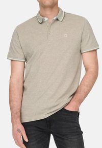 Beige Poloshirt mit einer dreiknopfigen Knopfleiste, kontrastierendem Kragen und Ärmelbündchen. Verfügt über ein kleines Logo auf der Brust und eine weiche Textur.