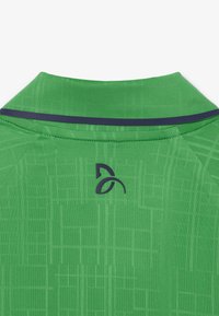 Camisa polo verde con un tejido texturizado y un sutil patrón de rejilla, un acento en el cuello de color marino y un logo oscuro en la parte posterior.