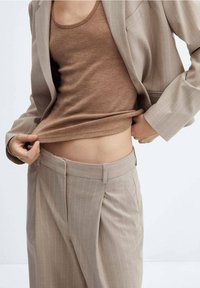 Débardeur moulant marron clair sous un blazer beige à fines rayures ; pantalon beige taille haute avec plis et poches latérales. Texture de tissu lisse.