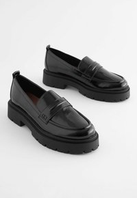 Zwarte lakleren loafers met een stevige zwarte platformzool, voorzien van een decoratieve band aan de voorkant en een ronde neusontwerp.