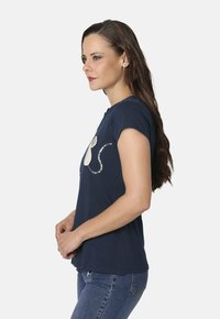 Camiseta de manga corta azul marino con un diseño de gato con lentejuelas en el frente. Tejido suave con un corte holgado, combinada con jeans de denim.