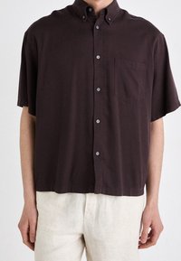 Korte mouwen, overhemd met knopen in donkerbruin katoen. Voorzien van een enkele borstzak en een relaxed fit met subtiele kraagdetails.
