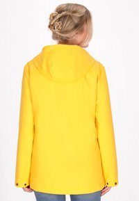 Gul vattentät jacka med en överdimensionerad huva, långa ärmar, dekorativt sömnad och knappstängning vid ärmsluten. Bakvy.