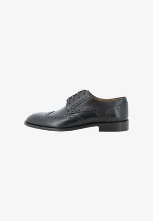 Scarpa elegante da uomo in pelle nera con dettagli brogue e allacciatura chiusa, mostrata su sfondo bianco.