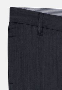 Pantaloni in tessuto blu scuro con una trama texturizzata, dotati di chiusura con bottone, passanti per la cintura e una fascetta interna a righe in contrasto.