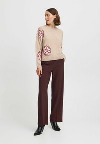 Pull beige avec broderie florale rose sur les manches, associé à un pantalons évasés marron foncé et des bottines à talons noires.