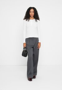 Un haut henley blanc à manches longues associé à un pantalon gris taille haute et un petit sac à main noir. Des chaussures bordeaux brillantes complètent le look.