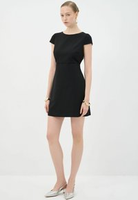 Vestido negro de manga corta con un torso ajustado y una falda acampanada, hecho de una tela suave. Combinado con zapatos slingback metálicos y pulseras doradas.