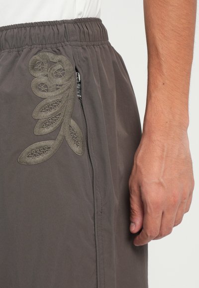Grå shorts med elastisk talje, sidelomme med lynlås og detaljeret grønt blomsterbroderi på venstre side.