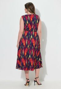 Värikäs, hihaton midi-mekko, jossa on elävä, monivärinen kuvio. Kevyestä kankaasta valmistettu, vyötärö on vyöhön sidottu ja hame on liehuva.