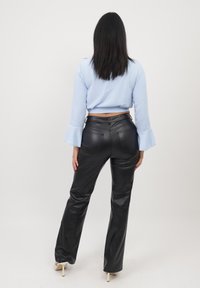 Pantalon en faux cuir noir avec une jambe évasée, associé à un haut court bleu clair avec des manches cloches, une ceinture visible et des poches arrière.