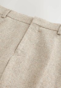 Beige tailored trousers made of textured fabric, featuring a flat front with neat stitch detailing and side pockets.