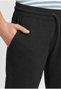 Zwarte katoenen joggers hebben een elastische tailleband, een trekkoord en zijzakken, met een soepele textuur en een losse pasvorm.