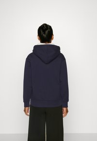 Sweat à capuche bleu marine avec une grande capuche, des poignets côtelés et une coupe décontractée. Il possède une doublure intérieure douce et un design uni. Pantalon noir à jambes larges.