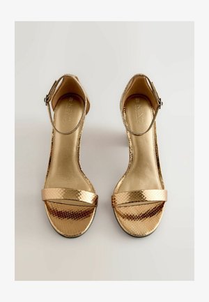 Gyldne højhælede sandaler med et tekstureret skindsnakemønster. Har ankelrem, to brede frontbånd og et skinnende gyldent indre.