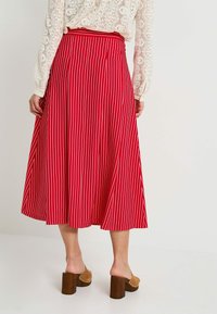 Falda midi a rayas rojas y blancas con cintura fruncida, que presenta un diseño fluido y un dobladillo que cae por debajo de las rodillas.