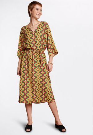 Langes, locker sitzendes Kleid aus gelbem Stoff mit einem wellenförmigen roten und grünen Muster. Es hat einen V-Ausschnitt und einen passenden Gürtel in der Taille.