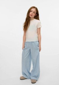 Vit kortärmad topp med scallop- kanter och ett litet runt mönster, tillsammans med blårandiga vida byxor. Texturerade beige tofflor.