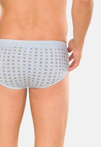 Slip blu con motivo che presentano un elastico azzurro chiaro, disegni geometrici in diverse tonalità di blu e grigio, realizzati in un morbido tessuto elasticizzato.