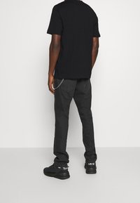 Černé bavlněné tričko s krátkými rukávy, kombinované s tmavě šedými džíny s řetízkovým detailem. Černé tenisky s bílými akcenty dokončují outfit.