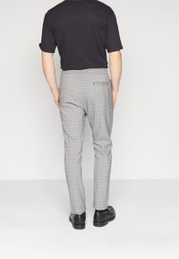 Šedé kostkované kalhoty z látky, s přizpůsobeným střihem, zúženými nohavicemi a zadní kapsou. Kombinovány s černými botami.