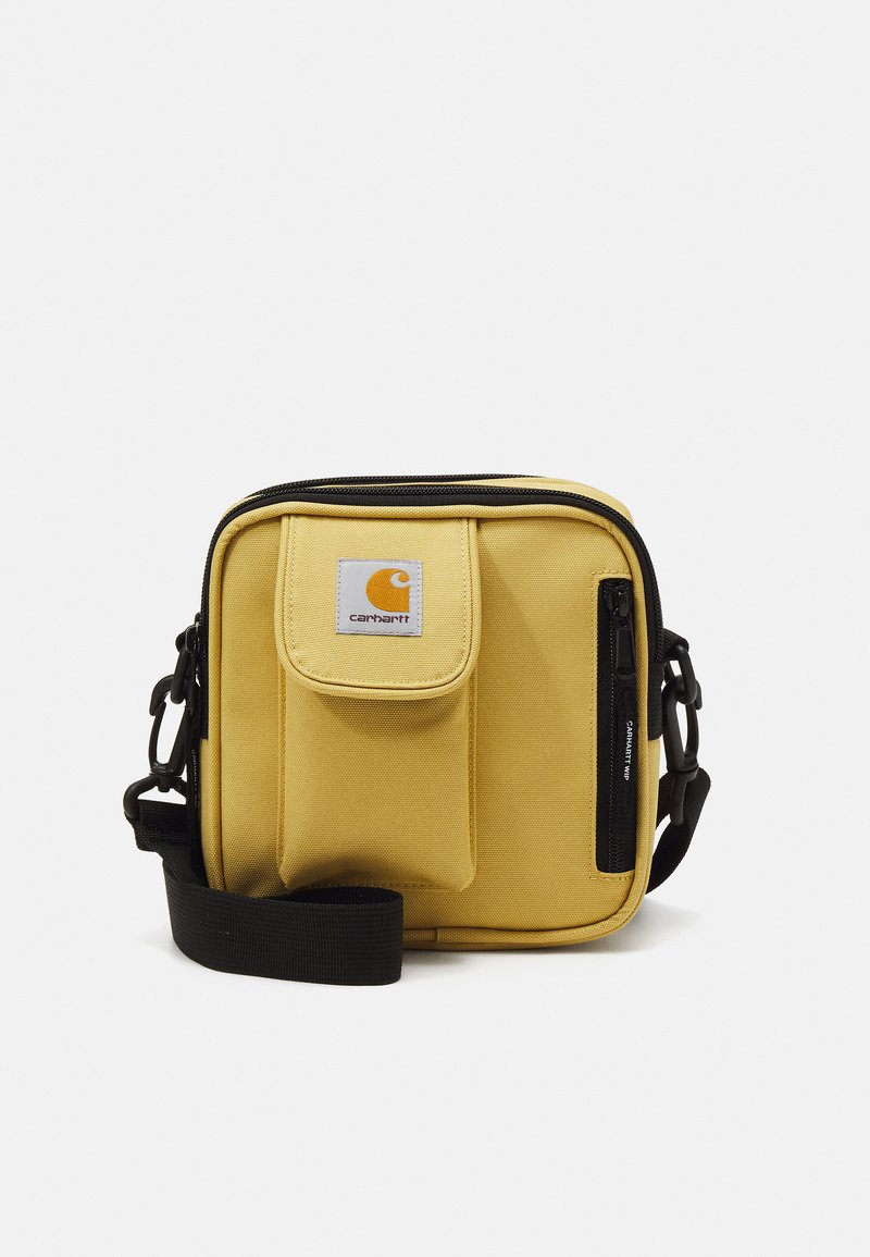 Borsa a tracolla gialla in tela con tasca frontale a pattella, dettaglio in zip nera, tracolla regolabile e patch logo bianco. Forma compatta e squadrata.