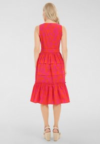 Robe sans manches rose vif avec un ourlet en volants superposés, un motif texturé et une taille ajustée. Dotée d'une fermeture éclair dissimulée au dos et d'un tissu doux.