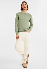 Lichtgroene langemouwen trui, crèmekleurige broek en beige enkellaarsjes. Casual fit met een eenvoudige ronde hals en geribde manchetten.