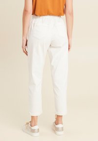Weiße Hosen mit umgeschlagenem Saum, einem elastischen Bund und aufgesetzten Taschen, kombiniert mit weißen Sneakern mit Glitzerdetails.