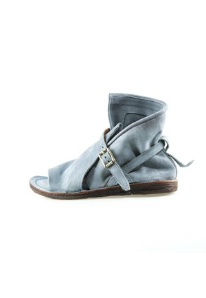 Bottine ouverte à bout ouvert en daim bleu clair avec une bride à boucle latérale et un petit talon en bois sur fond blanc.