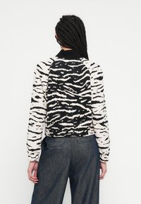 Veste courte avec imprimé animal noir et blanc, dotée d'un col noir et d'une ceinture élastique. Le matériau semble lisse avec des manches longues.
