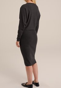Robe tricotée gris foncé avec une silhouette ajustée, des manches longues et une texture côtelée ; portée avec des chaussures plates noires, montrant une longueur en dessous du genou.