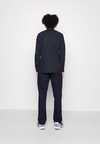 Tmavě modrá košile s dlouhým rukávem a přiléhavým střihem, s manžetami na knoflíky a jemným leskem, doplněná o odpovídající tmavé kalhoty a vzorované tenisky.