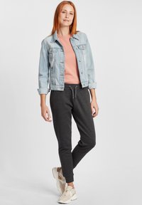Hellblaues Jeansjacke, pinkes T-Shirt und dunkelgraue Jogginghosen mit elastischen Bündchen. Beigefarbene Sneaker mit Strukturmuster. Lässiges Outfit.