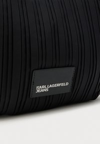 Fekete, rakott szövet táska, sima bőr címkével, amin fehérrel van domborítva a „KARL LAGERFELD JEANS” felirat. Texturált felszín, függőleges redőkkel.