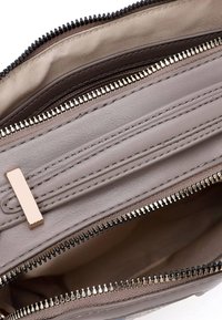 Grijze leren handtas interieur met twee ritsvakjes, voorzien van een gestructureerd oppervlak en een accent van goudkleurige hardware.