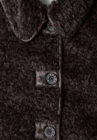 Gros plan d’un manteau en laine texturée brun foncé avec des boutons assortis cousus sur des empiècements en cuir le long de l’ouverture avant.
