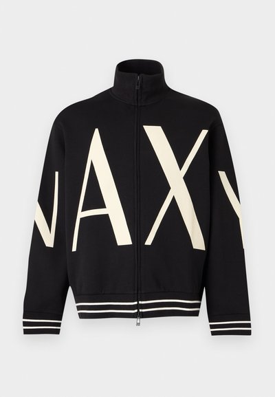 Veste noire zippée à col montant avec de grandes lettres crème "NAXY" sur le devant et les manches, avec poignets et bas rayés blancs.