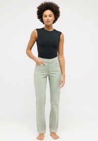 Svart ermeløs bodysuit kombinert med lysegrønne, høyt liv flared jeans, med frontlommer og en jevn, myk tekstur.