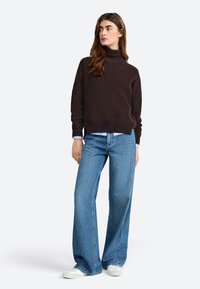 Dark brown ribbed turtleneck sweater paired with light blue wide-leg jeans and white sneakers. Simple design with a relaxed fit.