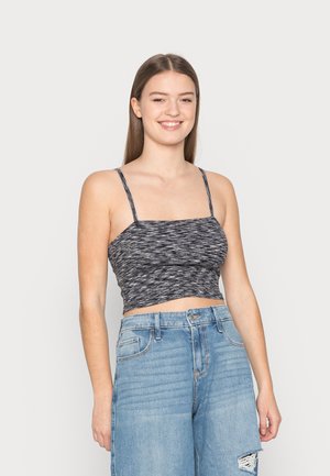Top cropped listrado em preto e branco com alças finas, apresentando um corpo ajustado e tecido texturizado. Combinado com jeans de denim azul de cintura alta.